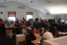 Office workers collaborate around a table as charts suggest steady business growth.